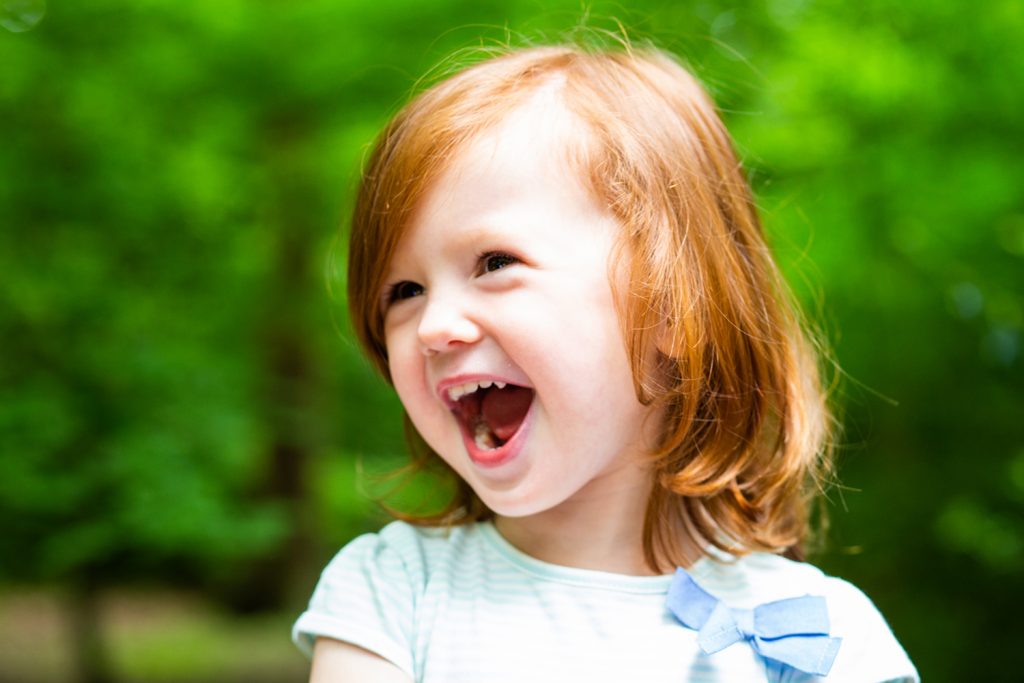 Red haired little girl laughing in front of trees