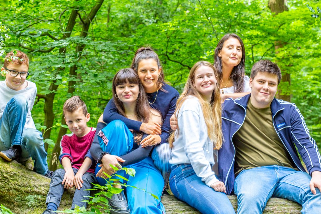 A group of children and teenagers sitting together on a fallen tree trunk, hugging and laughing