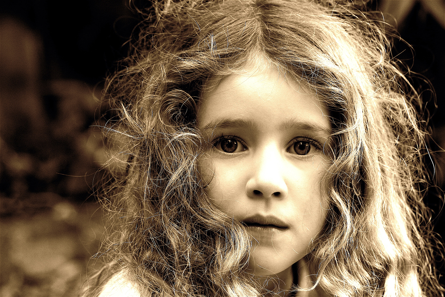 Black and white photo of little girl with long curly hair staring into the camera