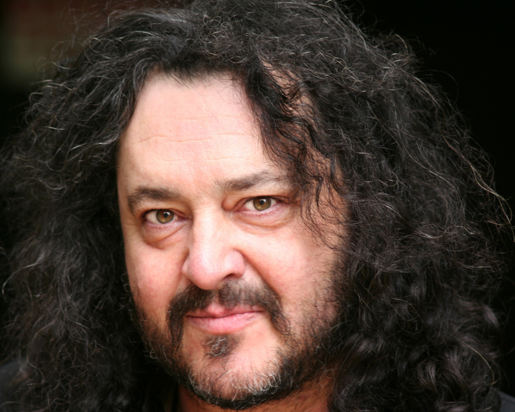 Middle-aged actor with long curly hair and dark beard looking at the camera