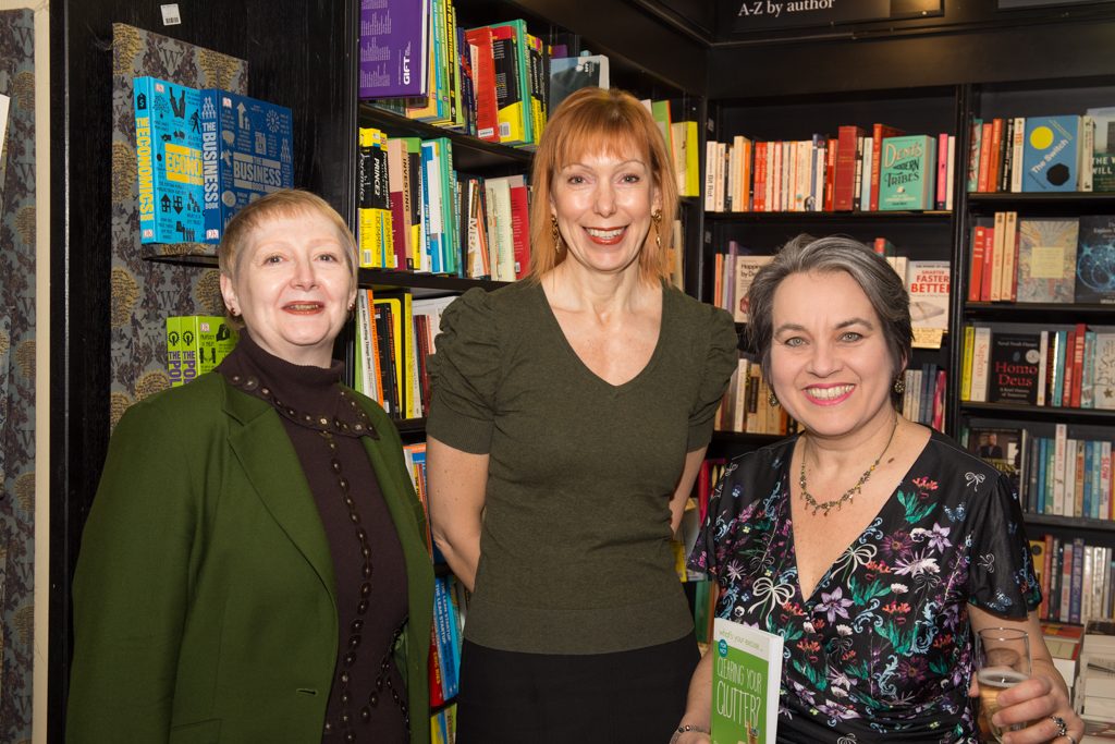 Three smiling women standing in front of book shelves at book launch