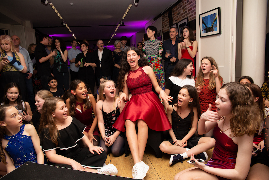 Lots of girls singing together sitting on the floor at Batmitzvah party