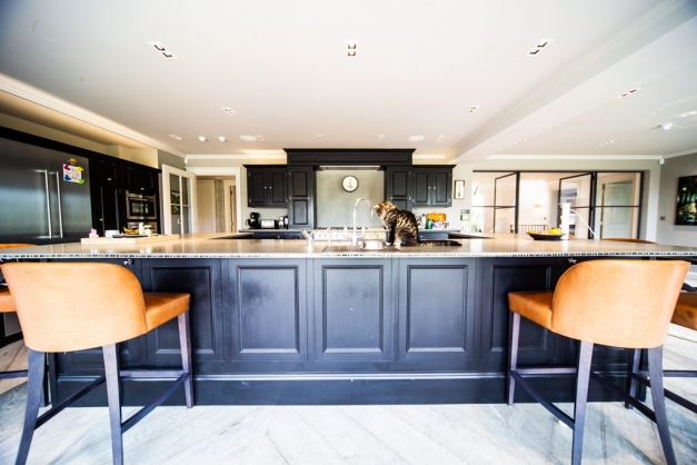 huge kitchen with dark blue cabinets and high chairs against breakfast bar. Cat sitting on top drinking from the tap