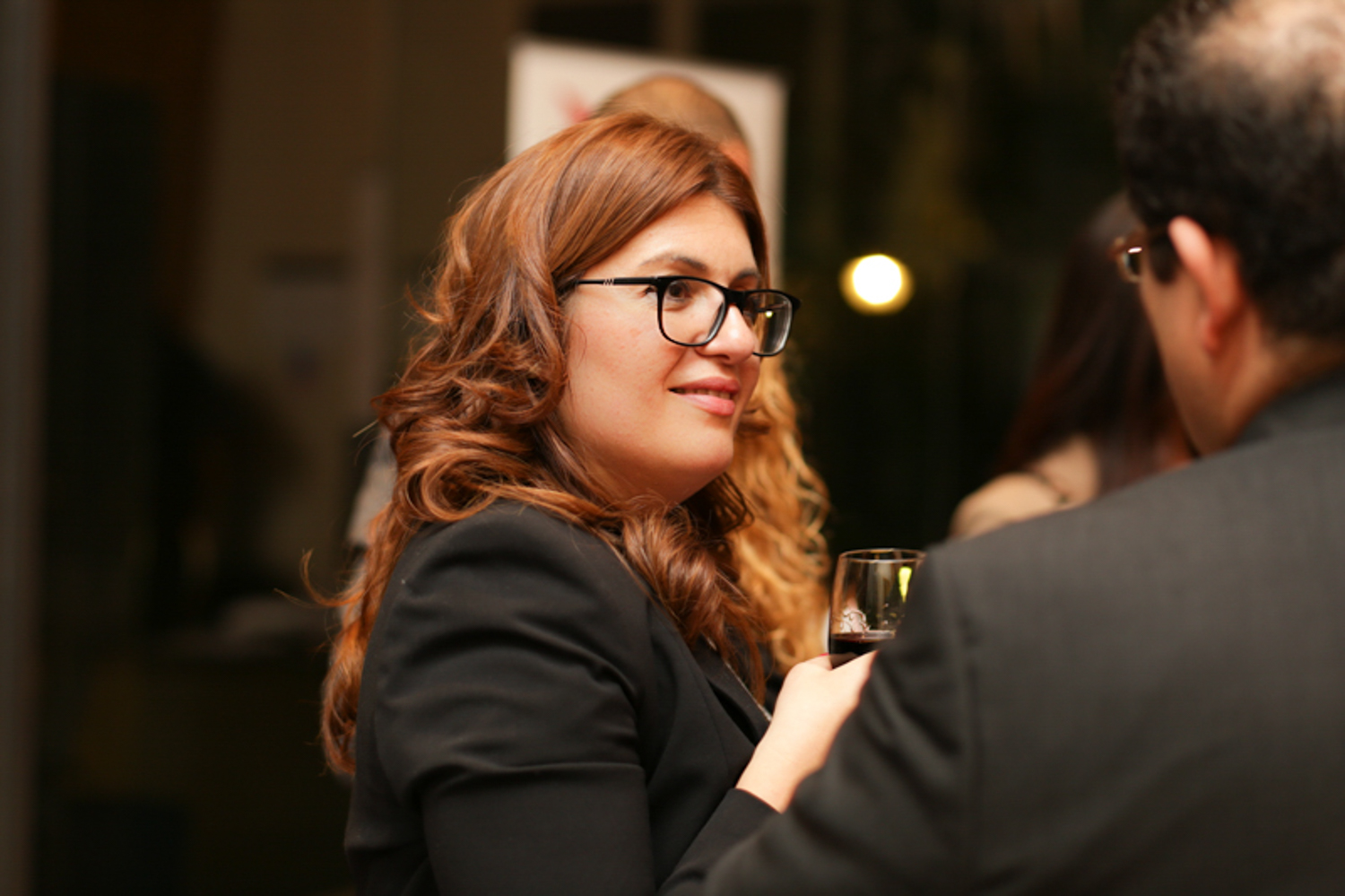 Lady with long brown hair holding glass of wine talking to a man at a business event