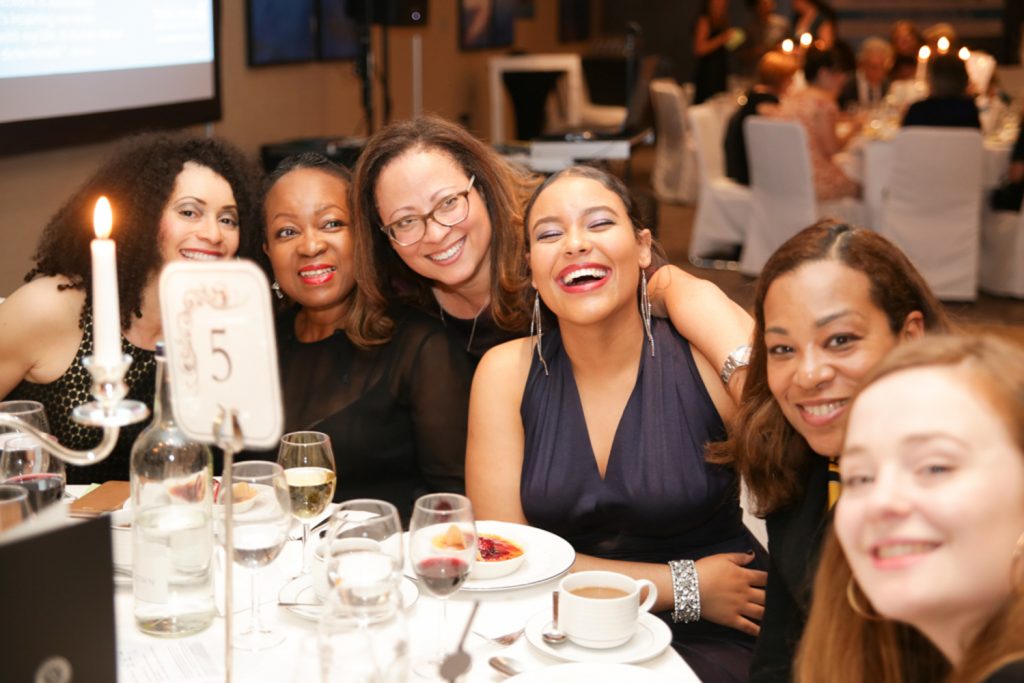 women sitting at a table at corporate event smiling into the camera