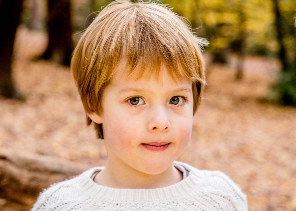 Little boy in the woods wearing cream wool jumper