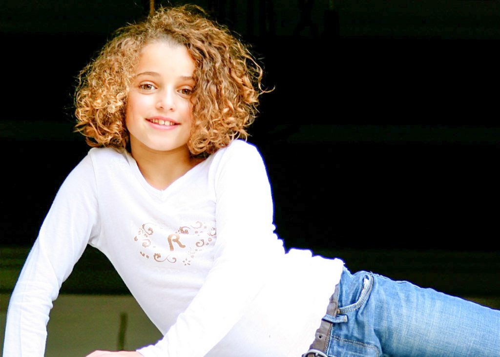 young teenage girl with ringlets wearing jeans and a t-shirt lying on her side smiling at the camera