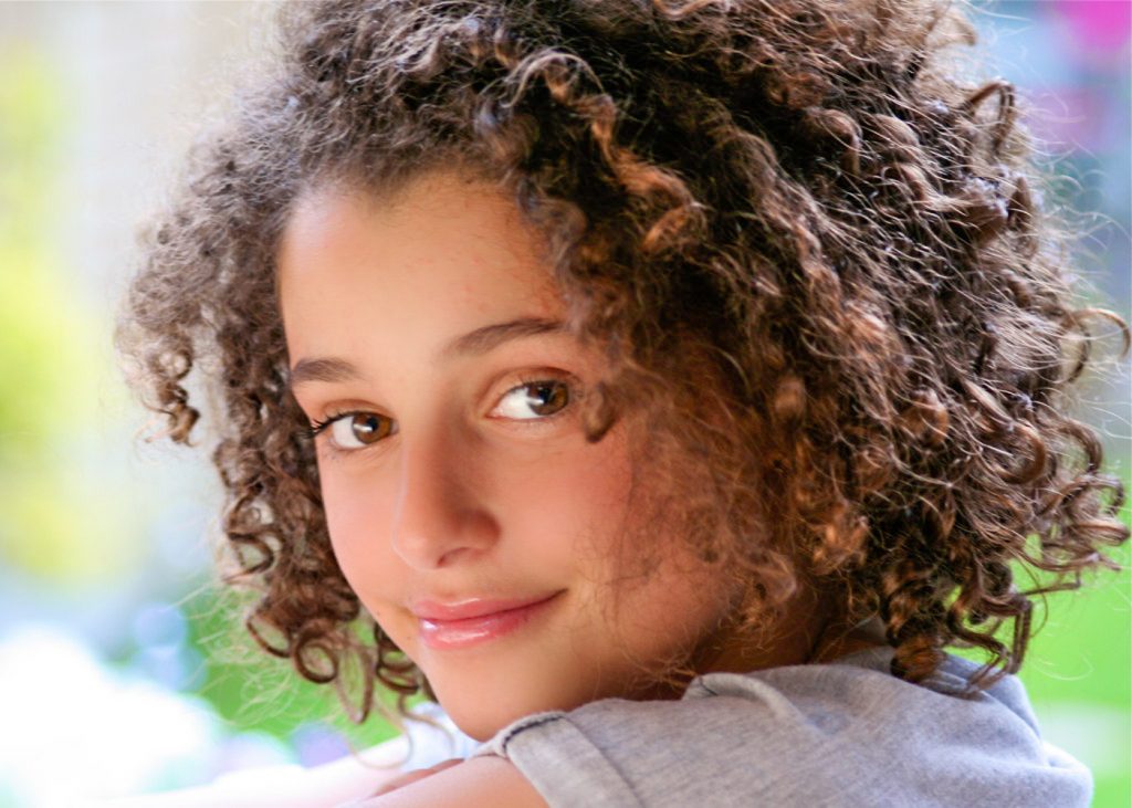 Teenage girl with curly brown hair smiling at camera