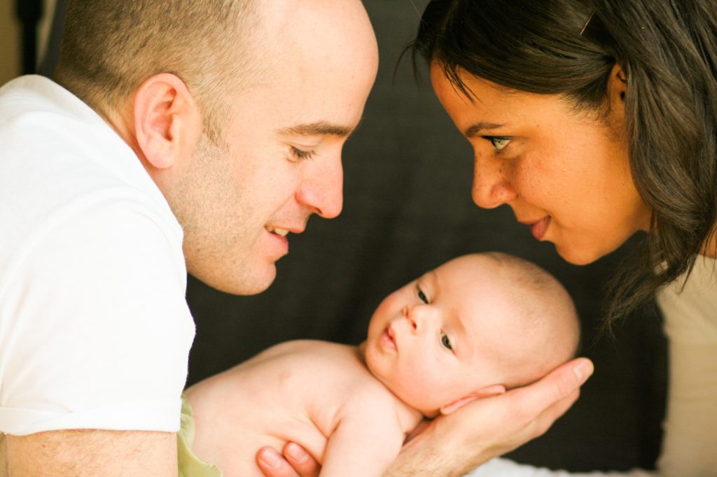 Young couple both holding and looking at new born baby