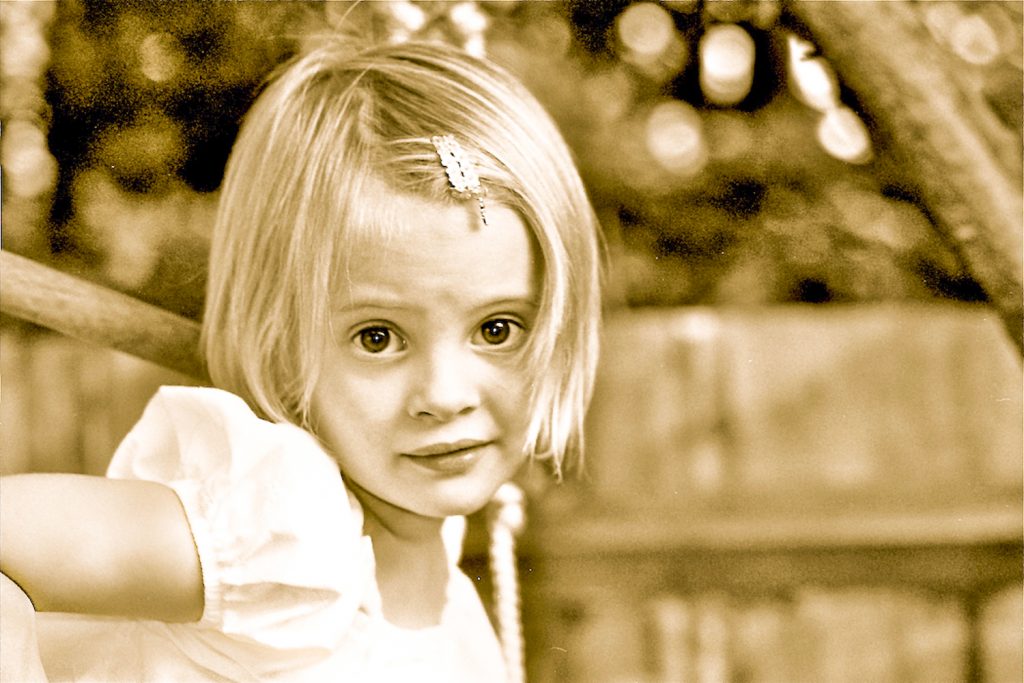 sepia image of young girl with short blond hair with a clip in her hair looking at camera