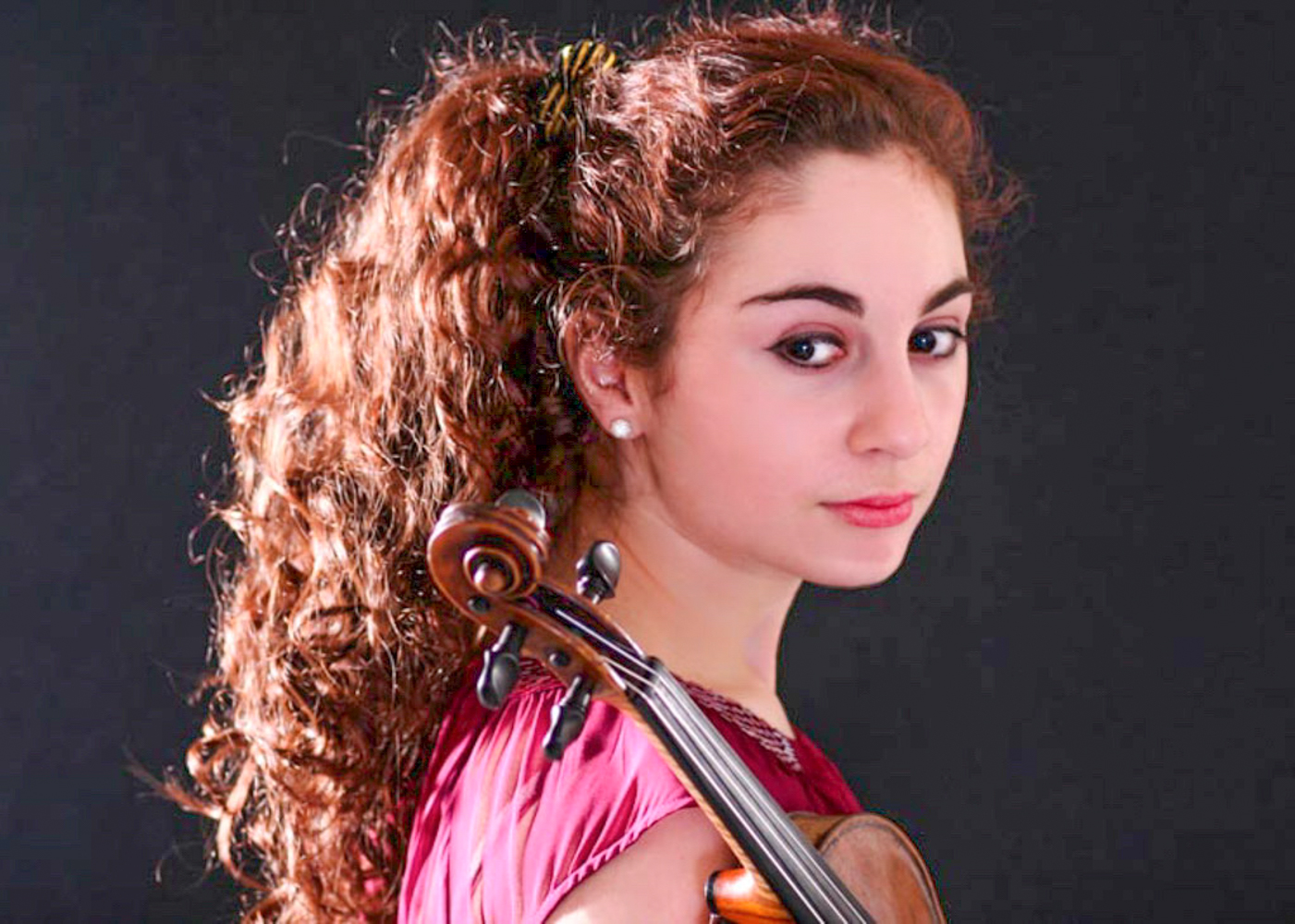 Headshot of young lady with long curly brown hair holding violin