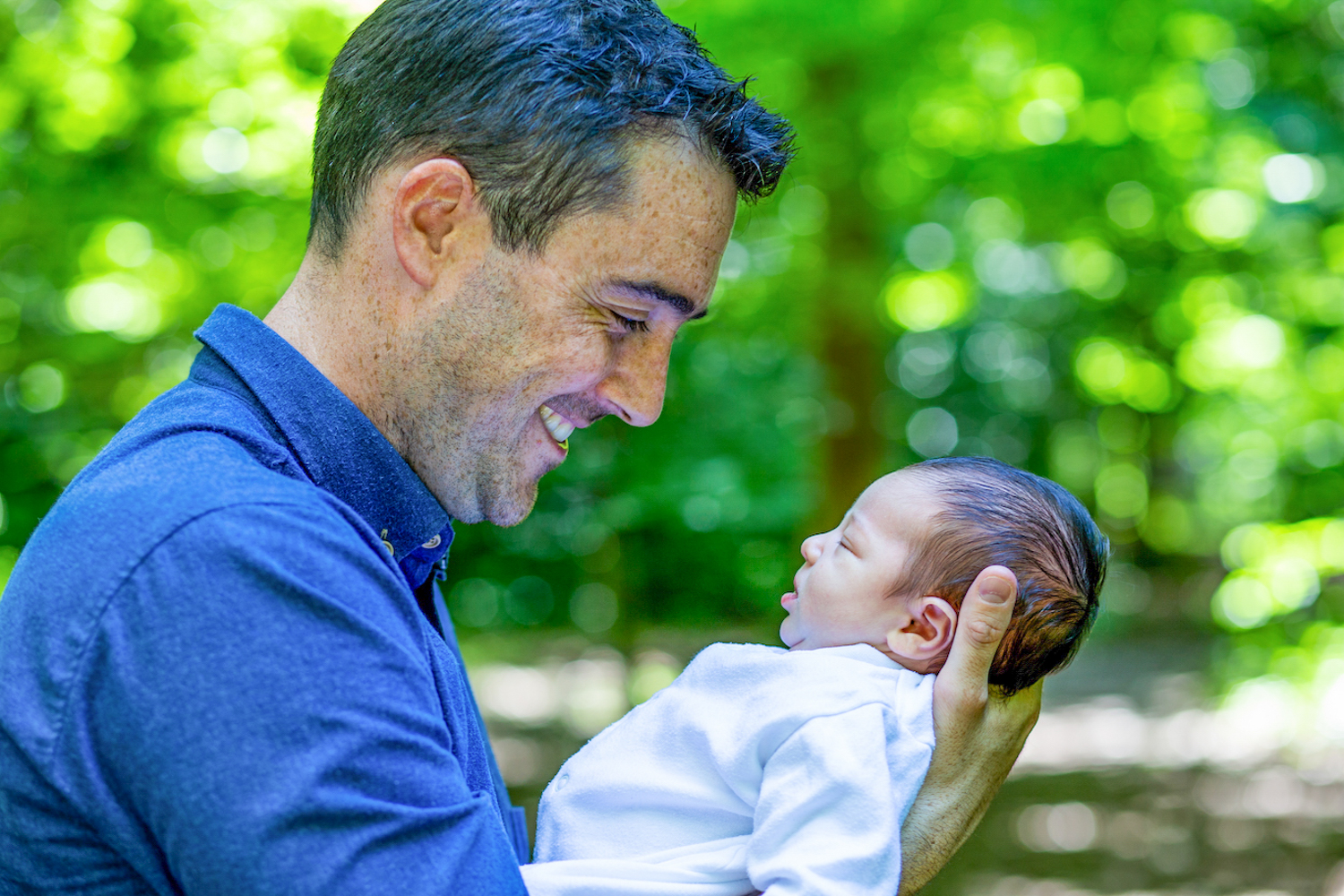 Man in blue shirt gazing at new born baby in the garden