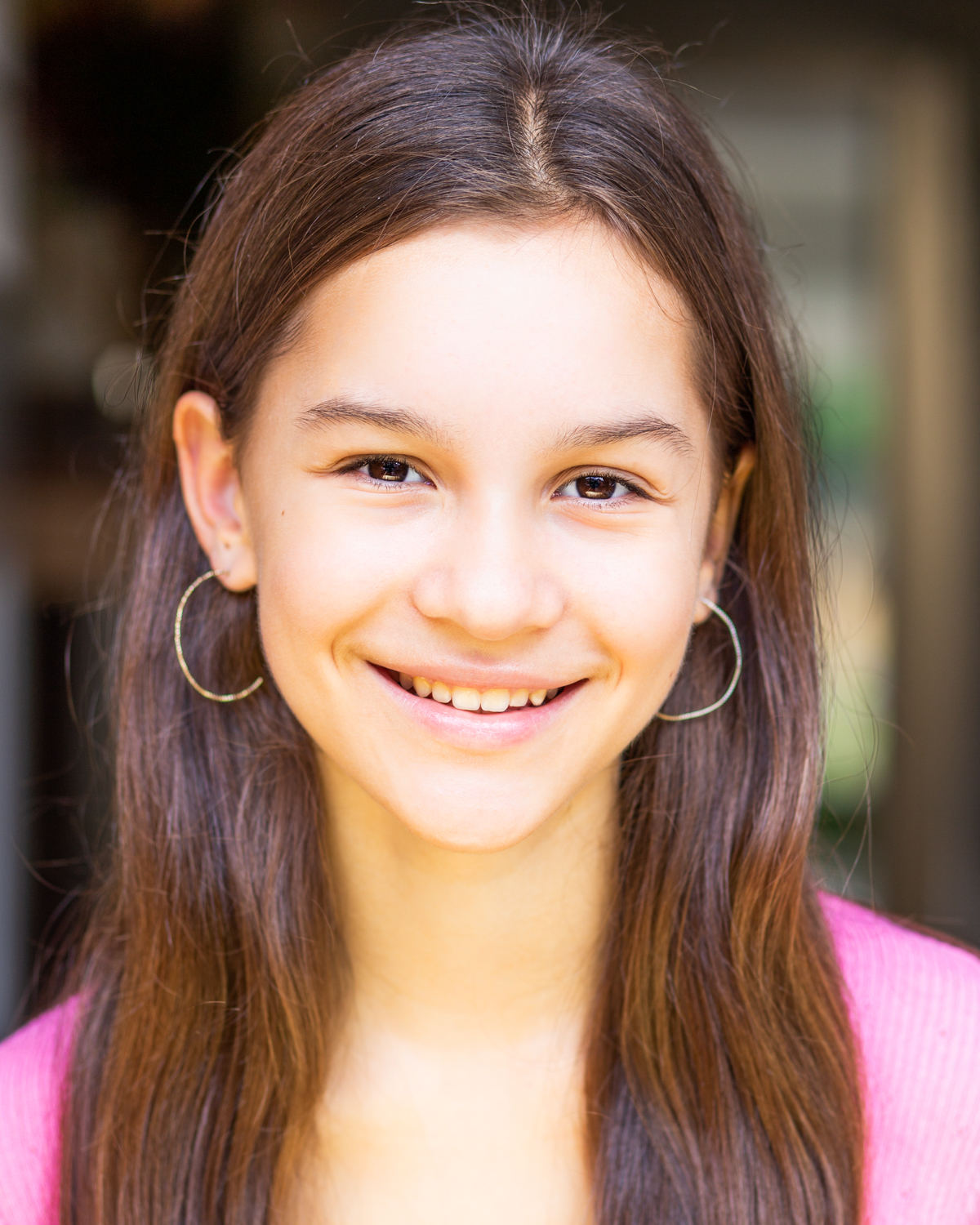 Teenage girl smiling at the camera wearing a pink top and big hoop earrings