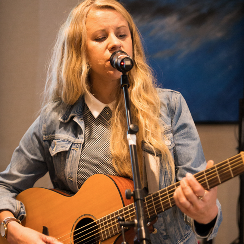 Blonde girl singing into a mic while playing the guitar