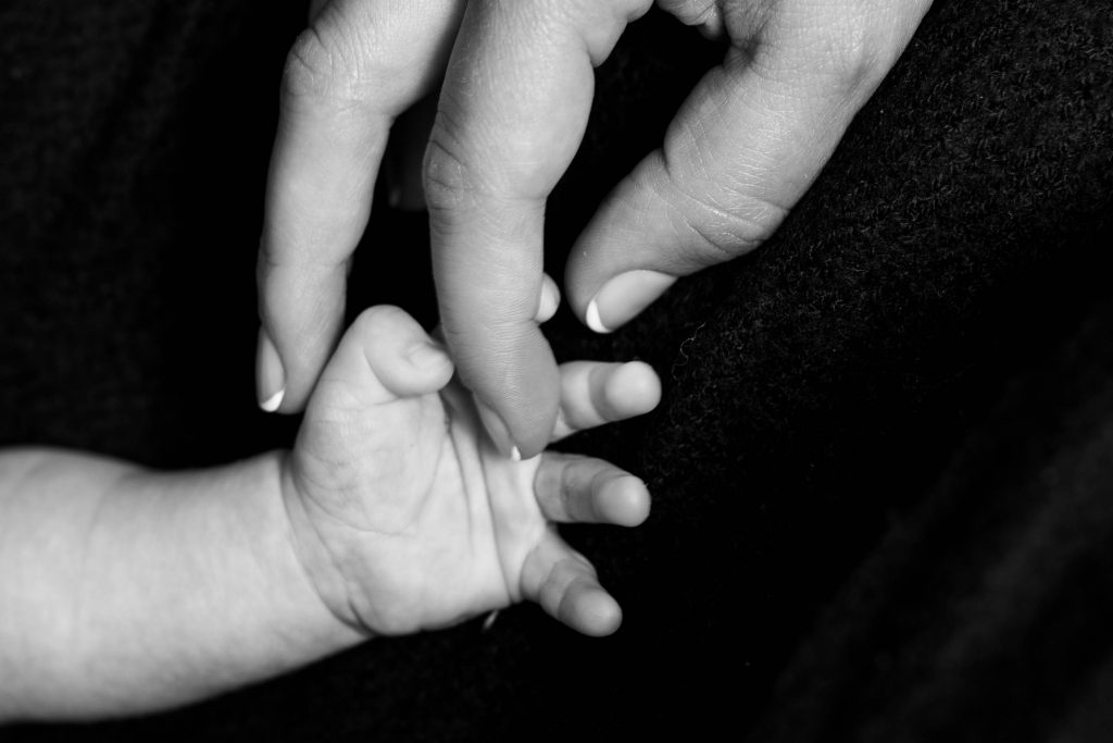 Black and white photo of woman's hand holding onto her baby's hand